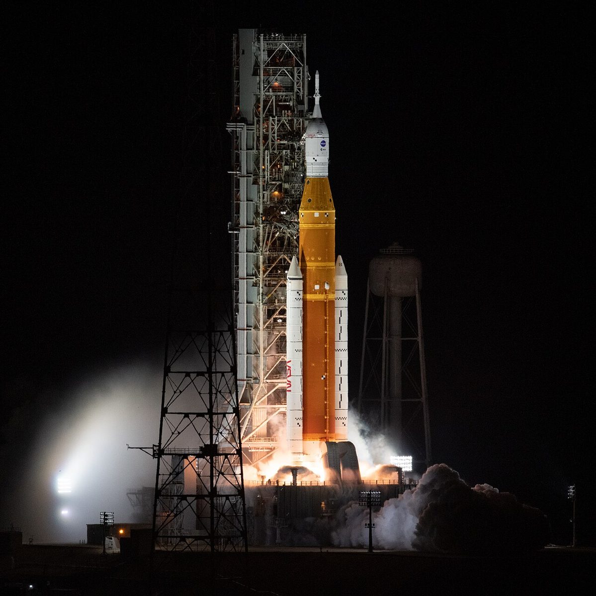 NASA's SLS rocket lifts off at night from Launch Pad 39B, lighting up the tower and the steam around it.
