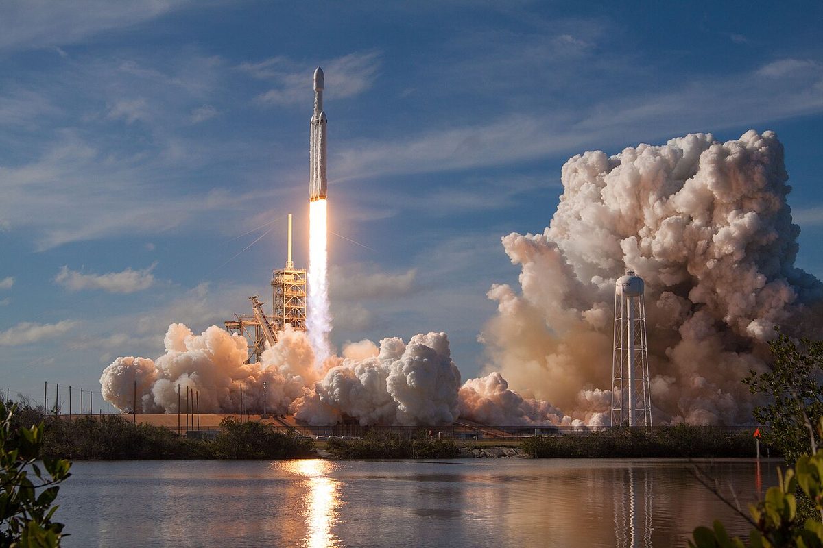 The Falcon Heavy rocket lifts off from its pad at Kennedy Space Center, its flame reflected in the water.