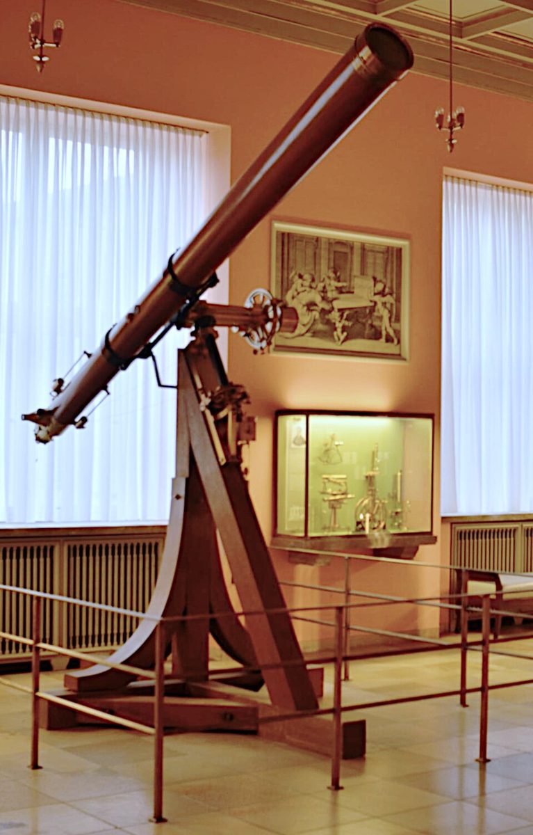 A long brass and wood refracting telescope on a wooden mount in a museum hall.