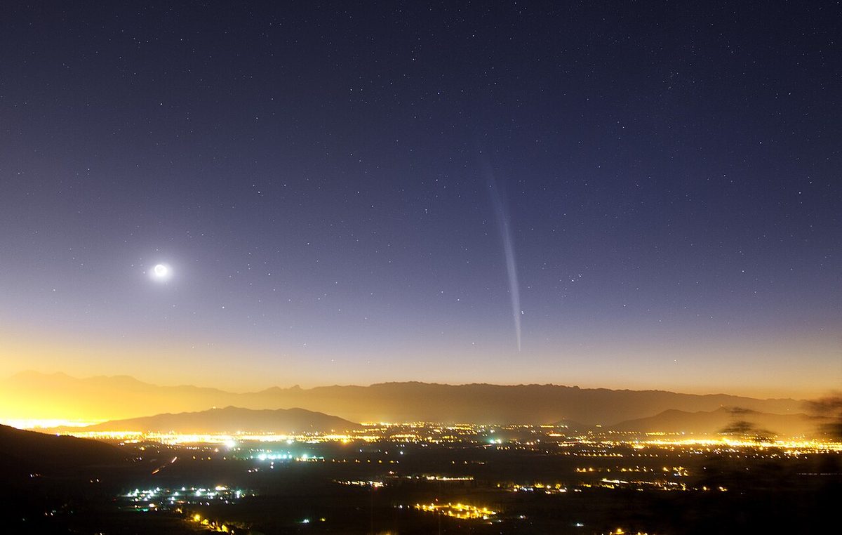 Comet Lovejoy's long thin tail rises from the dawn horizon above the lights of Santiago, with the Moon to the left.
