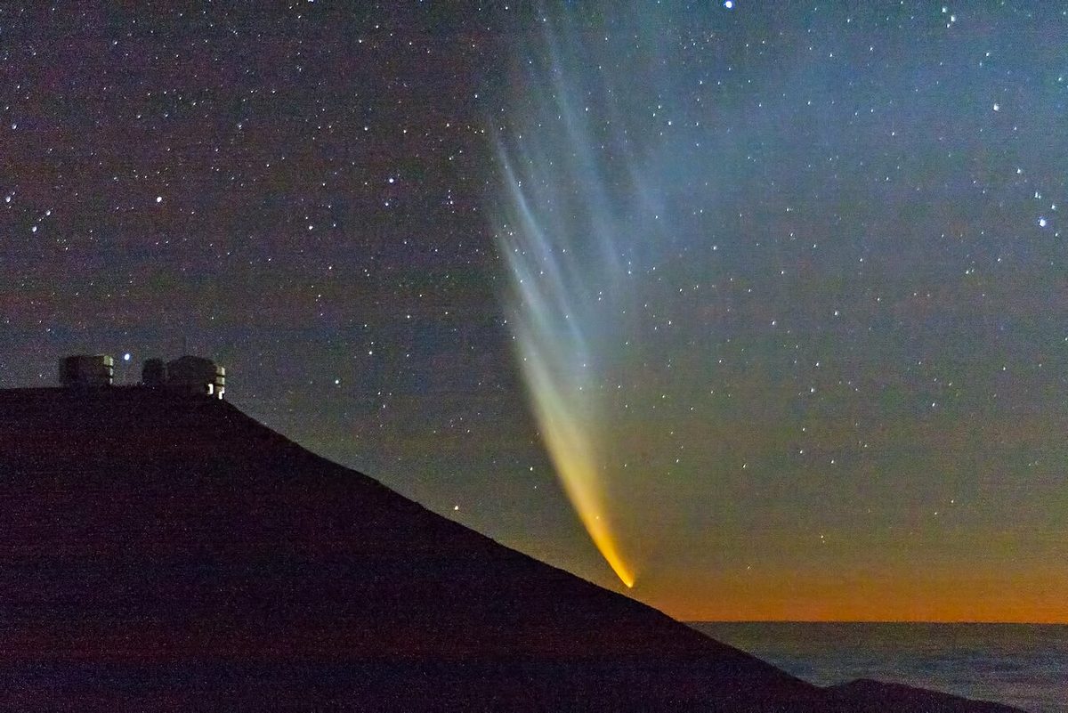 Comet McNaught's broad, striped tail fans up over the Pacific after sunset beside the telescopes of Paranal Observatory.
