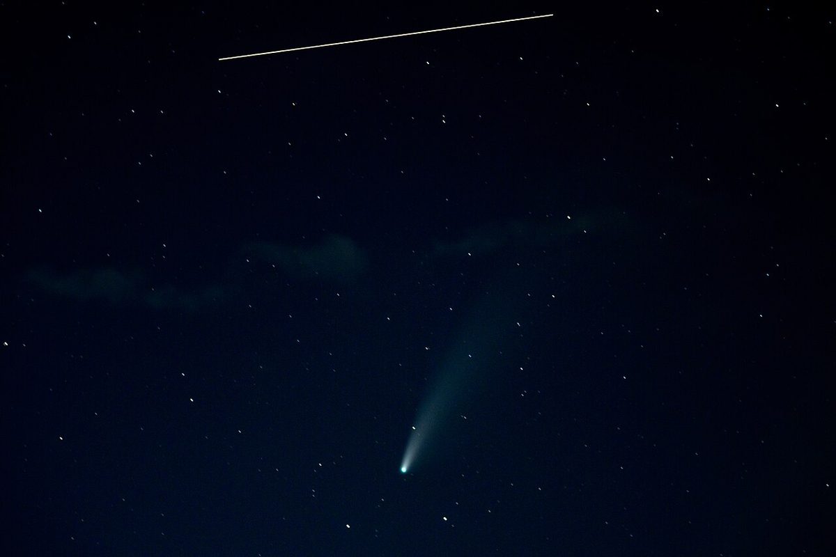 Comet NEOWISE with its curved tail low in a starry sky, with the International Space Station streaking past above it.