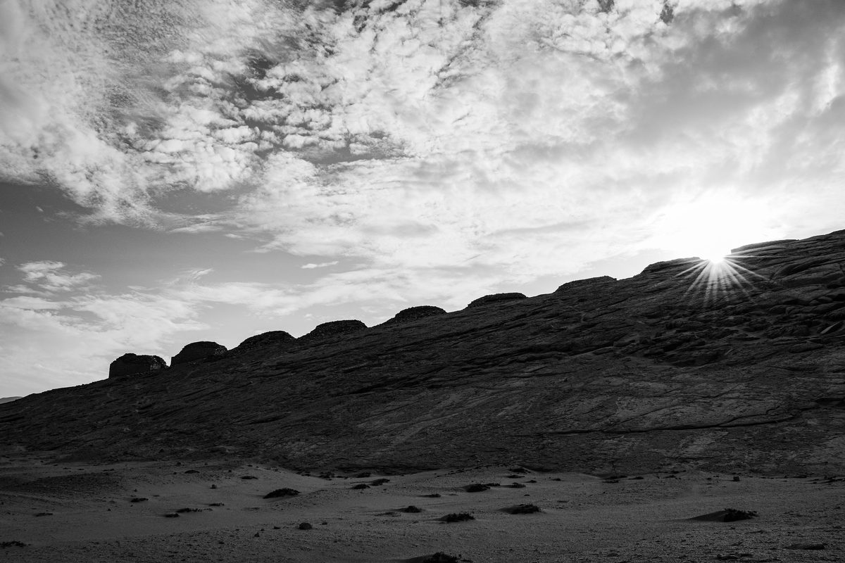 The Sun rises over the ridge beside the row of ancient towers at Chankillo, in black and white.