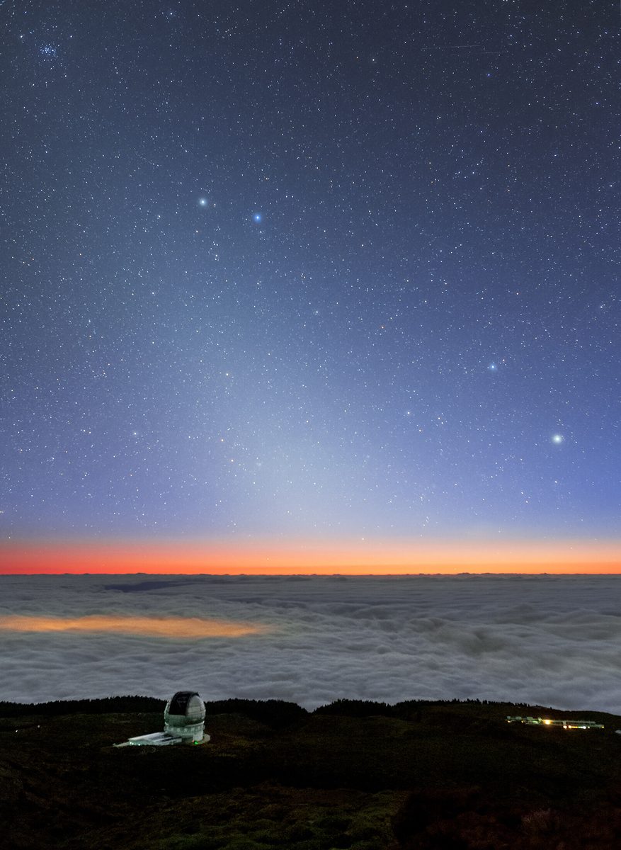 A faint cone of zodiacal light rises from the twilight above a sea of clouds and the Gran Telescopio Canarias dome on La Palma.