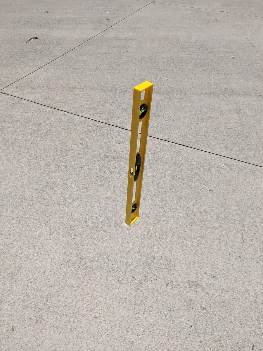 A builder's level stands upright on a Honolulu sidewalk at Lāhainā Noon and casts almost no shadow.