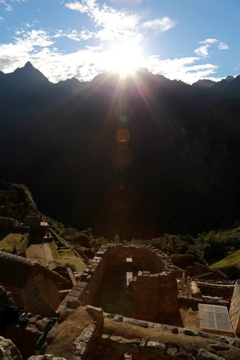 The solstice Sun rises over the Andes above the curved stone Temple of the Sun at Machu Picchu.