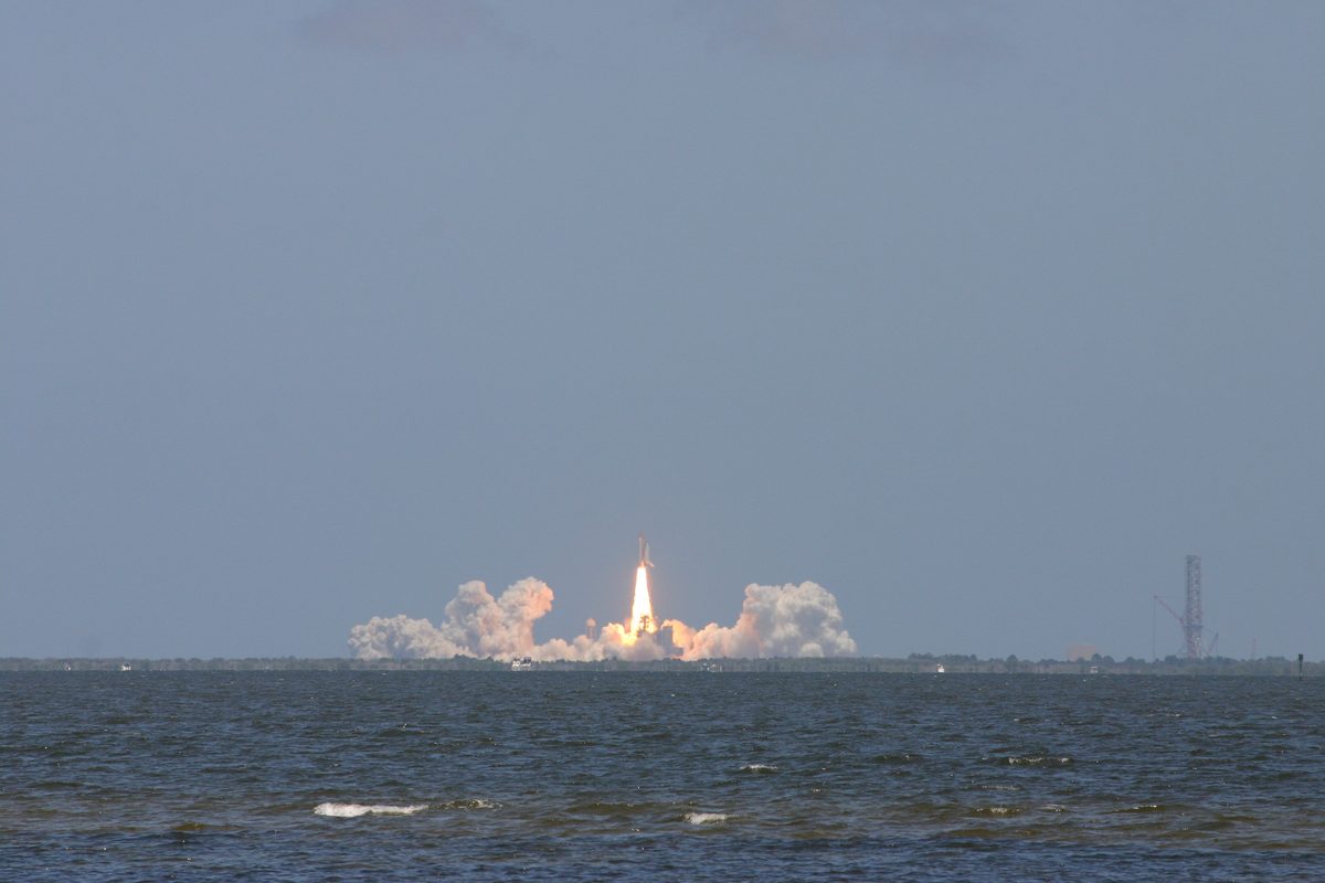A Space Shuttle rises on a column of fire and smoke from the Kennedy Space Center, seen across the Indian River from Titusville.