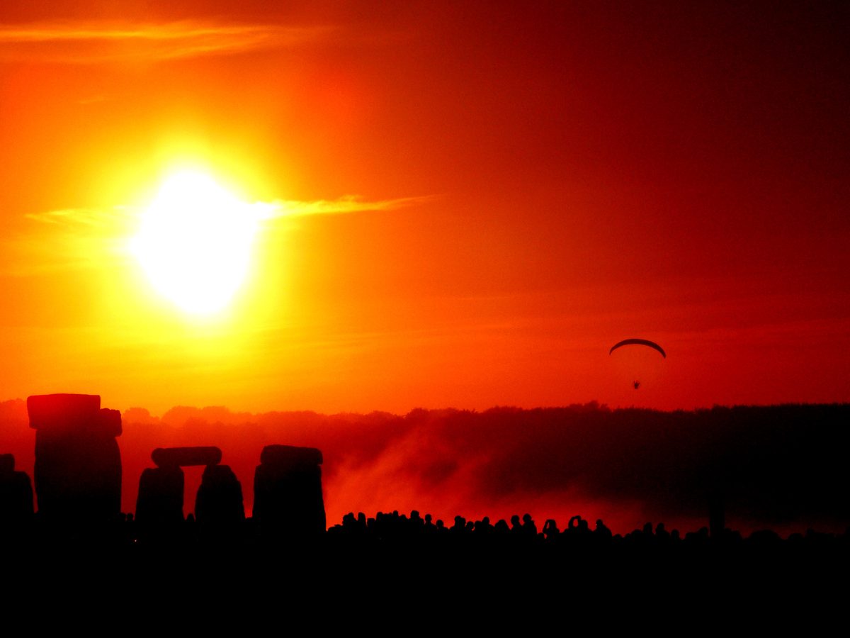 The rising Sun glows red over the silhouetted stones of Stonehenge and a crowd gathered at dawn.