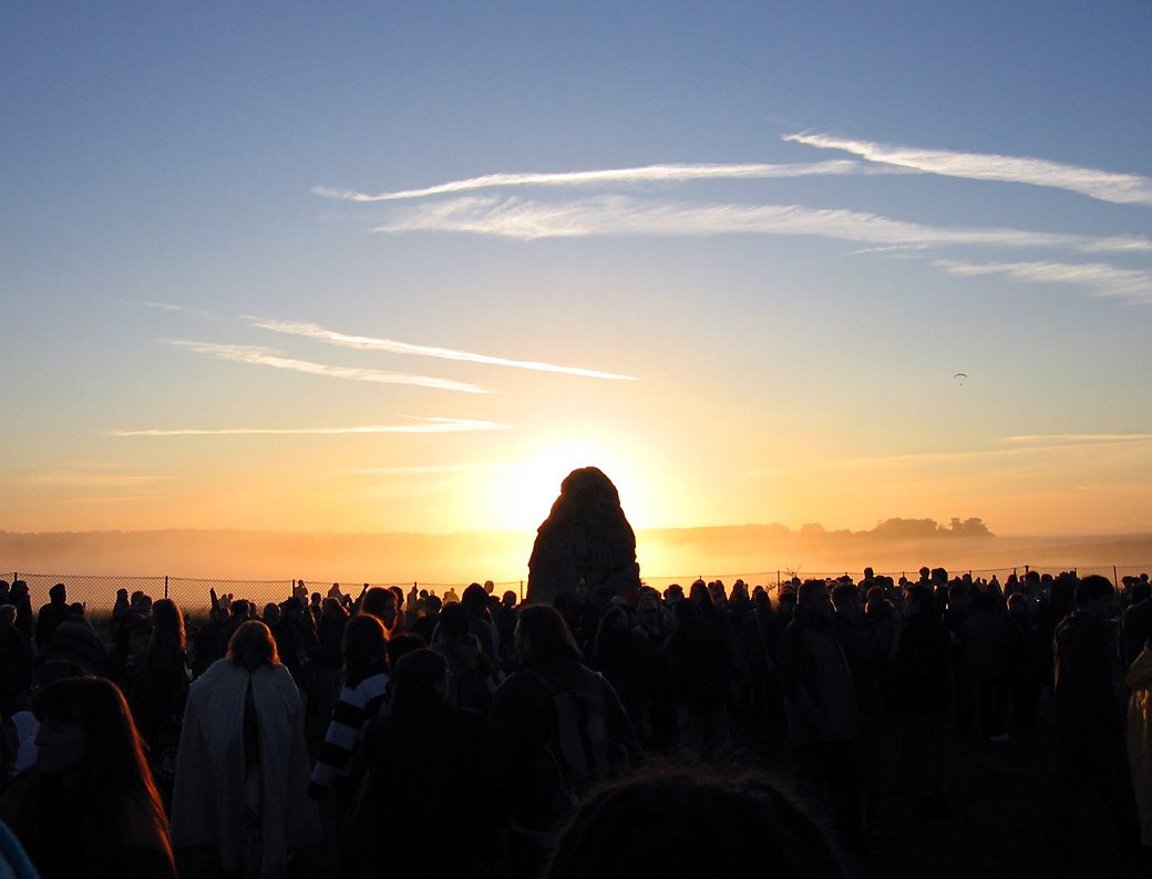 The Sun rises behind the Heel Stone at Stonehenge as a crowd watches on the summer solstice.